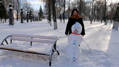 Joven-mujer-edificio-muñeco-de-nieve-en-el-parque.-En-el-invierno