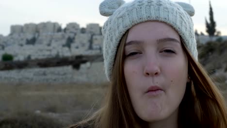 Portrait-of-a-beautiful-girl-in-a-knitted-cap,-which-showing-and-eating-Israeli-peanut-snacks-Bamba,-outdoor,-stock-footage.