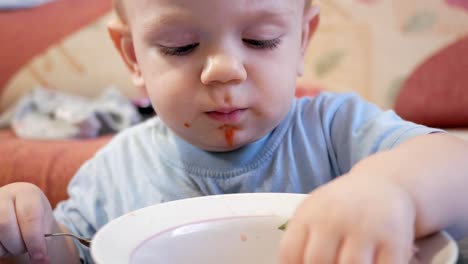 Un-atractivo-chico-de-2-años-de-edad-es-comer-sopa-roja-sí-mismo.-La-hoja-de-laurel,-atrapado-en-una-placa-y-el-niño-juega-con-él