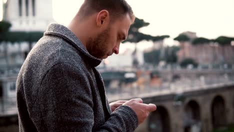 Stylish-man-stands-at-the-centre-of-Rome,-Italy.-The-handsome-male-uses-smartphone,-browse-the-Internet