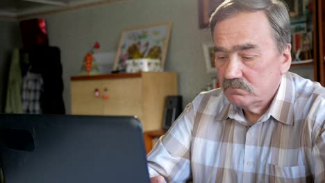 An-elderly-man-with-a-mustache-sits-behind-a-laptop-and-solves-problems.-He-looks-seriously-at-the-monitor