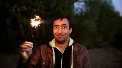 Portrait-of-young-smiling-man-with-sparkler-celebrating-at-beach-party