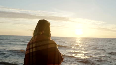 Back-view-of-the-brunette-woman-standing-on-the-shore-of-sea-and-dreaming.-Young-female-enjoying-the-beach-and-sunset