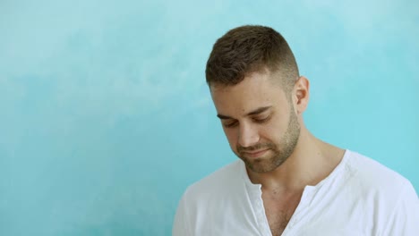 Portrait-of-young-man-smiling-into-camera-and-flirting-on-blue-background-concept