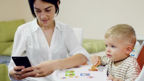 Mother-uses-phone-during-little-son-eating-biscuit