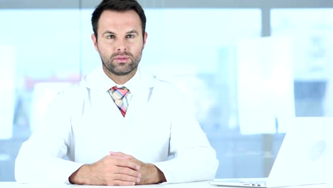 Portrait-of-Doctor-Looking-At-Camera-Sitting-in-Clinic