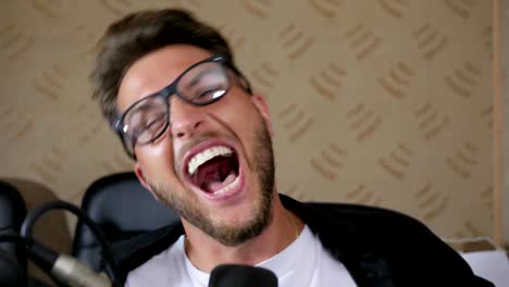 crazy-male-in-eyeglasses-with-wide-open-mouth-screams-into-microphone-indoors