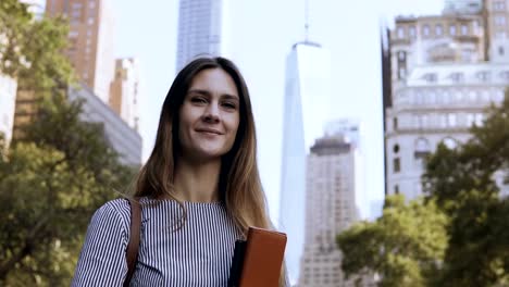 Portrait-of-young-businesswoman-holding-the-documents.-Female-looking-at-camera-and-gives-the-thumbs-up-in-New-York,-USA