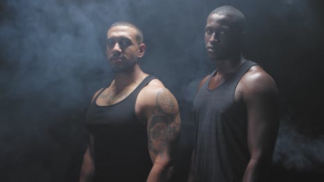 Portrait-shot-of-two-muscular-black-men-staring-at-the-camera-on-a-foggy-dark-background.