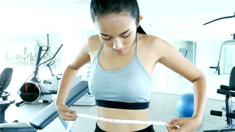 Asian-sport-girl-measuring-waist-with-white-ribbon.-Woman-exercise-at-fitness-gym.-Sport-and-Reaction-concept.-4k-Resolution.