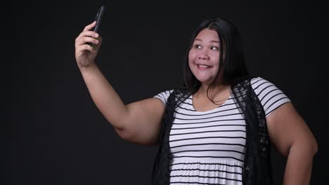 Beautiful-overweight-Asian-woman-using-mobile-phone-against-black-background