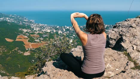 Sentarse-la-mujer-en-posición-de-loto-practicando-yoga-se-mueve-o-medita-y-levanta-sus-brazos-para-arriba-en-las-montañas