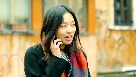 smiling-pretty-chinese-woman-talking-by-phone-in-the-street