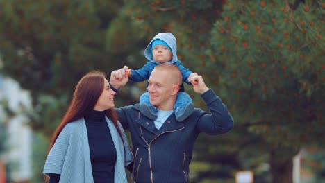 Dad-bears-his-son-on-his-shoulders.-Mom,-Dad-and-child-walk-together-in-the-park