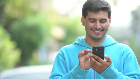 Glücklich-persischer-Jüngling-mit-Telefon-im-freien