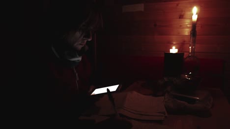 Woman-using-smartphone-hand-writing-paper,-candle-light-in-dark-room