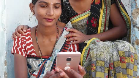 Tilt-to-two-beautiful-women-in-traditional-Rajasthani-local-dress-costume-sari-on-a-mobile-phone-sharing-a-photo-video-with-each-other-at-the-comfortable-of-their-home-face-portrait-cute-hands-closeup