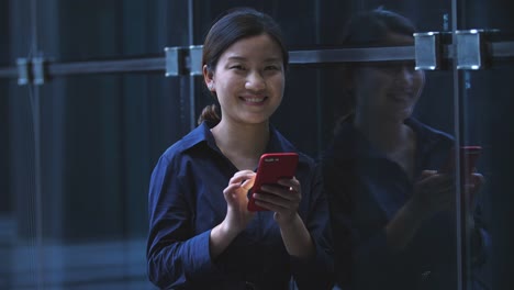 Young-Asian-Businesswoman-Using-Mobile-Phone-Leaning-the-Office-Window,--4k