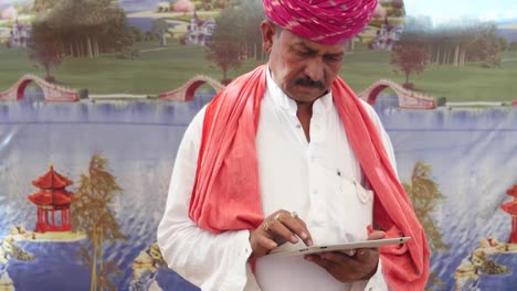 Handheld-Indian-man-busy-on-a-touchscreen-tablet-with-a-wonderfully-colourful-tent-backdrop