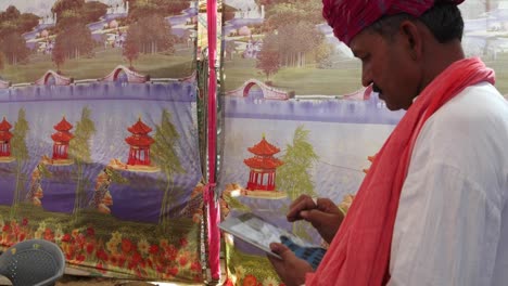 Handheld-Indian-man-busy-on-a-touchscreen-tablet-with-a-wonderfully-colourful-tent-backdrop