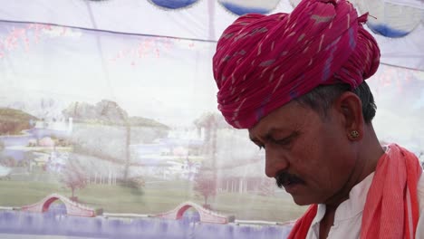 Handheld-Indian-man-busy-on-a-touchscreen-tablet-with-a-wonderfully-colourful-tent-backdrop