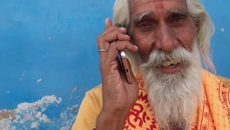 Handheld-Nahaufnahme-von-einem-Hindu-Sadhu-Lächeln-während-des-Besuchs-eines-Anrufs-auf-seinem-Handy