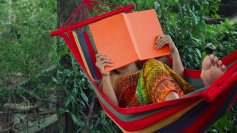 Young-woman-laying-down-on-hammock-and-reading-a-book