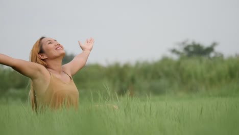 Joyful-Woman-Sitting-on-the-green-field-and-raising-her-hand-refresh-life