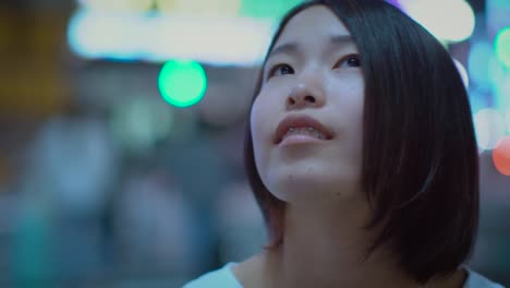 Portrait-of-the-Attractive-Japanese-Girl-with-Piercing-and-Wearing-Casual-Looks-around-Her-in-Wonder.-In-the-Background-Big-City-Advertising-Billboards-Lights-Glow-in-the-Night.