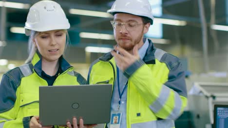 Macho-y-hembra-ingenieros-industriales-llevando-seguridad,-trabajo-en-una-planta-de-fabricación,-que-discutir-proyecto-mientras-Laptop.In-usando-la-planta-Industrial-de-fondo.