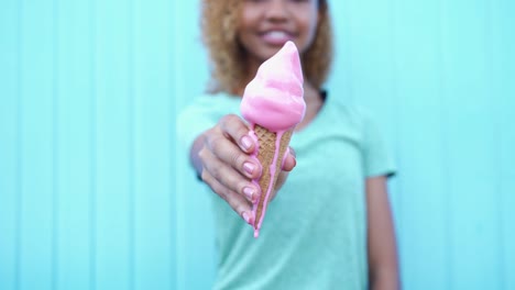 Glückliches-schwarzes-Mädchen-zeigt-Rosa-schmelzenden-Eis-dann-beginnen-zu-essen-am-blauen-Wand-Hintergrund