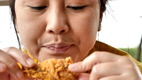 Close-up-Cute-asian-woman-are-happy-eating-fried-chicken-leg-in-restaurant.-Video-4k-Slow-motion