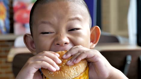 Cerca-niño-asiáticos-comer-hamburguesa,-lindo-muchacho-feliz-con-hamburguesa-en-el-restaurante.-Video-Slow-motion