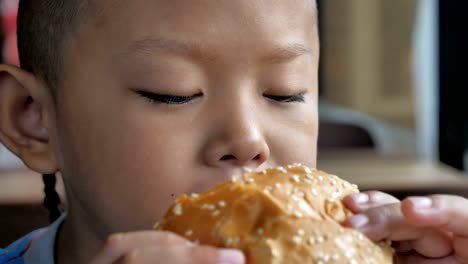 Close-up-little-asians-boy-enjoy-eating-burger,-Cute-happy-boy-holding-hamburger-at-restaurant.-video-Slow-motion