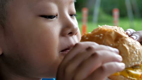 Cerca-niño-asiáticos-comer-hamburguesa,-lindo-muchacho-feliz-con-hamburguesa-en-el-restaurante.-Video-Slow-motion