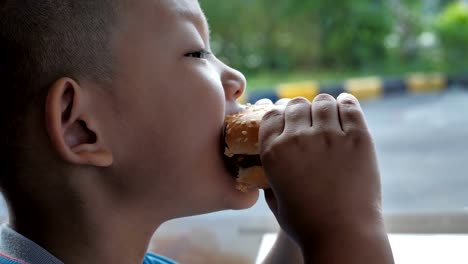 Close-up-little-asians-boy-enjoy-eating-burger,-Cute-happy-boy-holding-hamburger-at-restaurant.-video-Slow-motion