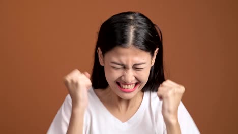 Finger-crossed-girl.-Young-asian-woman-in-white-t-shirt-standing-with-fingers-crossed-for-good-luck-and-finally-wins-isolated-on-orange-background.