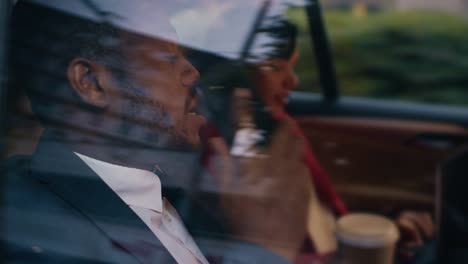 Businesswoman-and-Businessman-Riding-on-the-Backseat-of-a-Taxi-Cab-in-the-Evening.-Man-Makes-a-Phone-Call,-Woman-Works-on-a-Laptop.-Camera-Shot-made-from-Outside-the-Car.