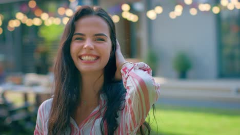 Retrato-de-hermosa-morena-con-el-pelo-suelto-sonriendo-encantadoramente,-enderezar-su-cabello.-En-el-fondo-caliente-día-de-verano-y-parte-del-jardín-en-el-patio-trasero.-En-cámara-lenta.