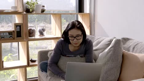 Schöne-Asiaten-junge-Frau-arbeiten-mit-Computer-Laptop-sitzend-auf-Sofa-zu-Hause.-Arbeit-zu-Hause-Konzept