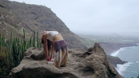 Chica-practicando-yoga-en-las-rocas-contra-el-cielo-azul-y-el-azul-del-mar.-Mujer-está-parado-en-una-piedra-en-una-postura-de-puente.
