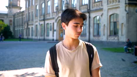 Bored-handsome-asian-male-is-looking-aside-and-looking-for-something-interesting,-standing-on-the-street-in-ancient-city