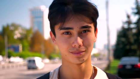 Close-up-beutiful-face-og-asian-guy-looking-at-camera-relaxed-and-standing-near-highway,-city-life,-warm-sunny-day