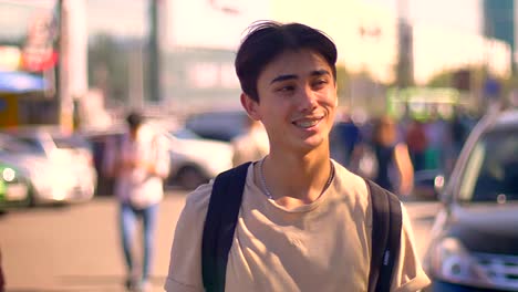 Happy-surprised-asian-boy-is-waving-on-the-street,-while-staying-near-road-with-cars-on-background