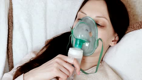 Verwenden-Sie-Vernebler-und-Inhalator-für-die-Behandlung.-Junge-Frau-Einatmen-durch-Inhalator-Maske-auf-der-Couch-liegen.-Seitenansicht.