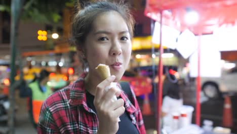 Junge-attraktive-Asiatin-genießen-Erdbeereis-im-Waffelhörnchen-abends-am-Nachtmarkt.