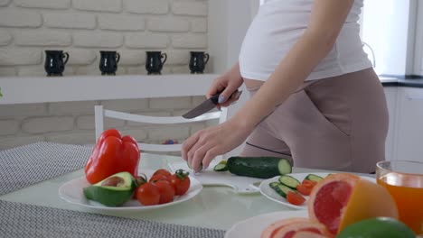 sana-futura-madre-con-vientre-grande-cocina-útil-apetitosa-ensalada-de-vegetales-frescos-para-el-almuerzo-en-la-cocina