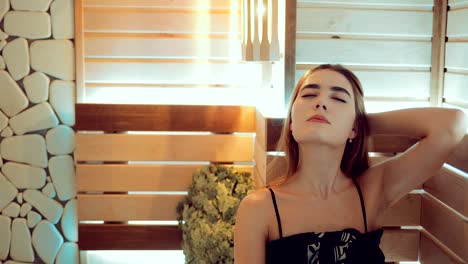 Young-beautiful-girl-touches-her-hair-in-the-sauna.-Girl-is-sitting-on-the-bench.-Portrait-view.