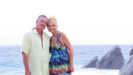 Una-Pareja-de-ancianos-sonriente-en-la-playa-con-olas-y-rocas-detrás-de-ellos