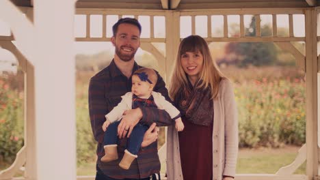 Portrait-of-an-attractive-young-family-under-a-gazebo,-dad-holding-the-baby,-at-a-farm-on-an-overcast-day